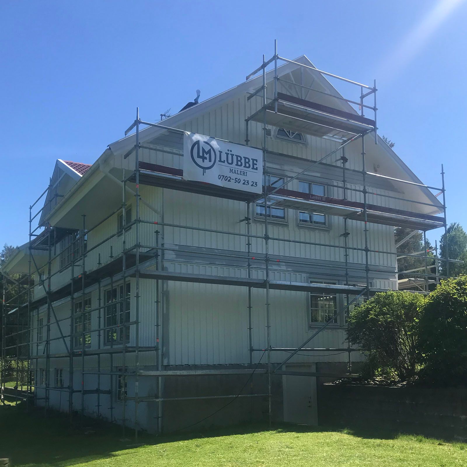 Villa med byggställning och Lübbe Måleris skylt under fasadmålning